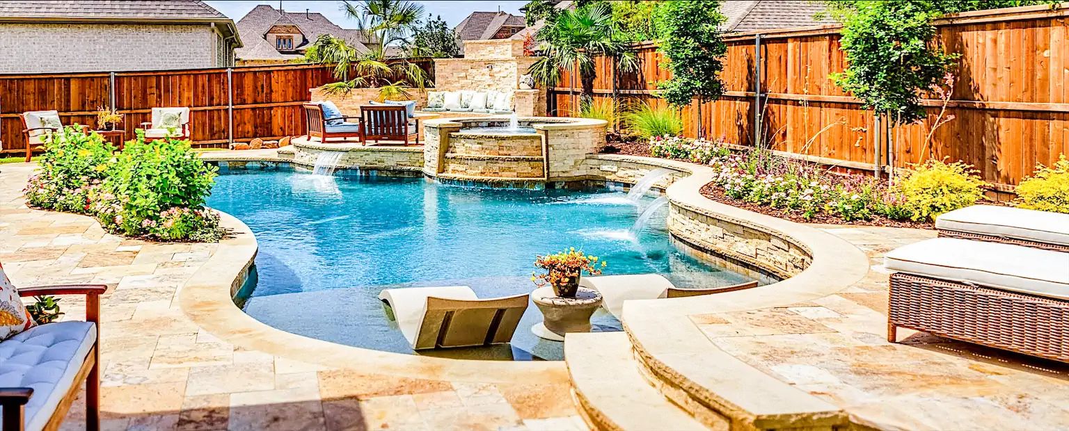 A freeform pool with a raised stone spa, scuppers, and in-pool loungers inside a wood-fenced backyard