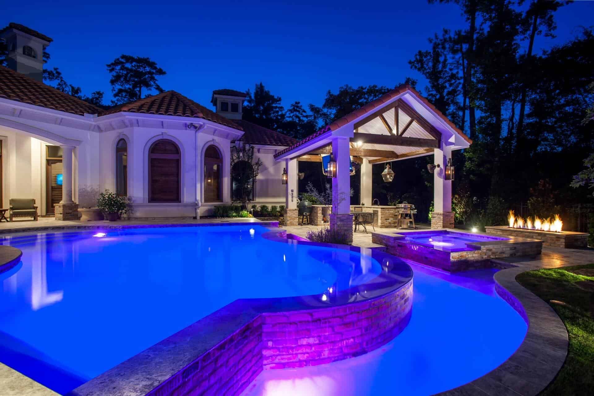 A freeform pool and raised spa glowing with LED lighting at night