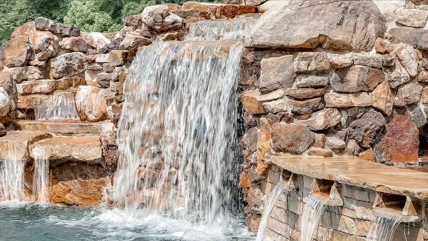 A stacked stone waterfall and scupper wall spilling into a pool
