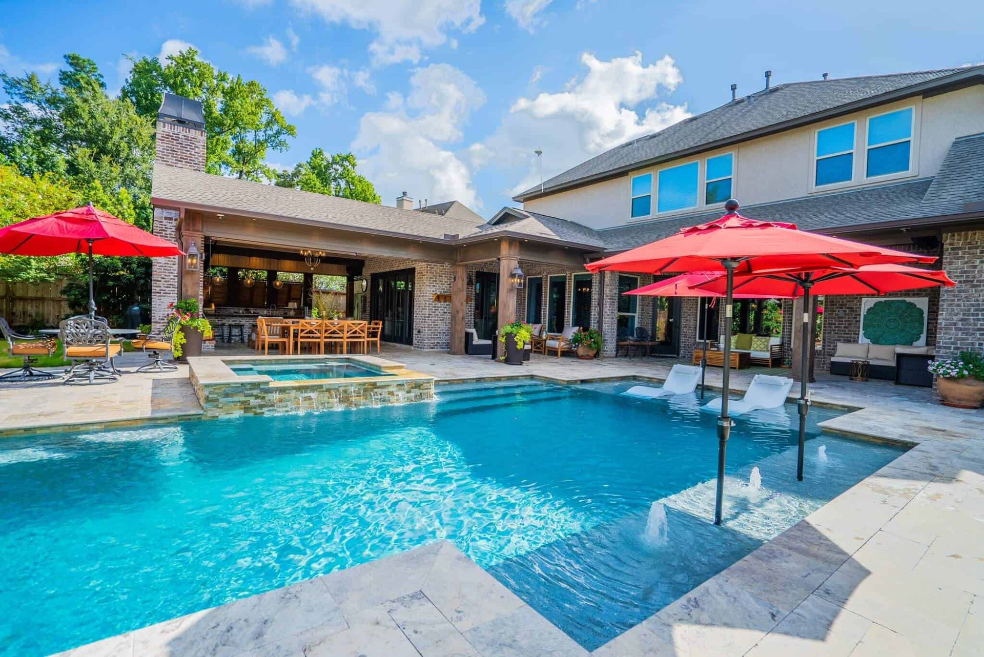 A sparkling pool with a tanning shelf and red umbrellas behind a two-story Texas home